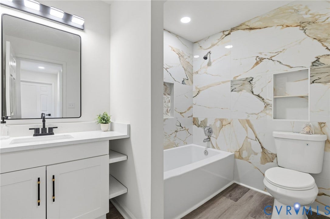 409 S Jefferson Street, Bolling, Petersburg, VA 23803 Spa-inspired primary bathroom featuring marble-look tile walls, a freestanding soaking tub, floating vanity with integrated storage, frameless mirror with integrated lighting, and a separate water closet