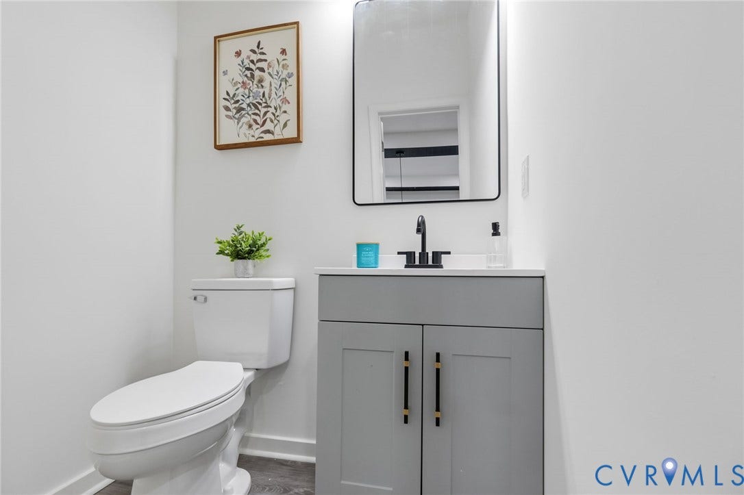 409 S Jefferson Street, Bolling, Petersburg, VA 23803 White toilet with a built-in tank, a gray vanity with double cabinet doors, a white countertop, and a rectangular black-framed mirror