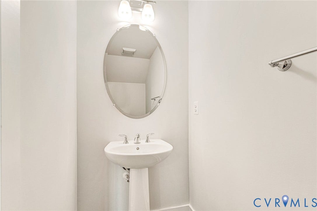 4347 Saunders Station Loop, #A, Glen Allen, VA 23233 Elegant half bath featuring a pedestal sink with chrome widespread faucet, oval framed mirror with integrated lighting, and soft neutral wall finishes