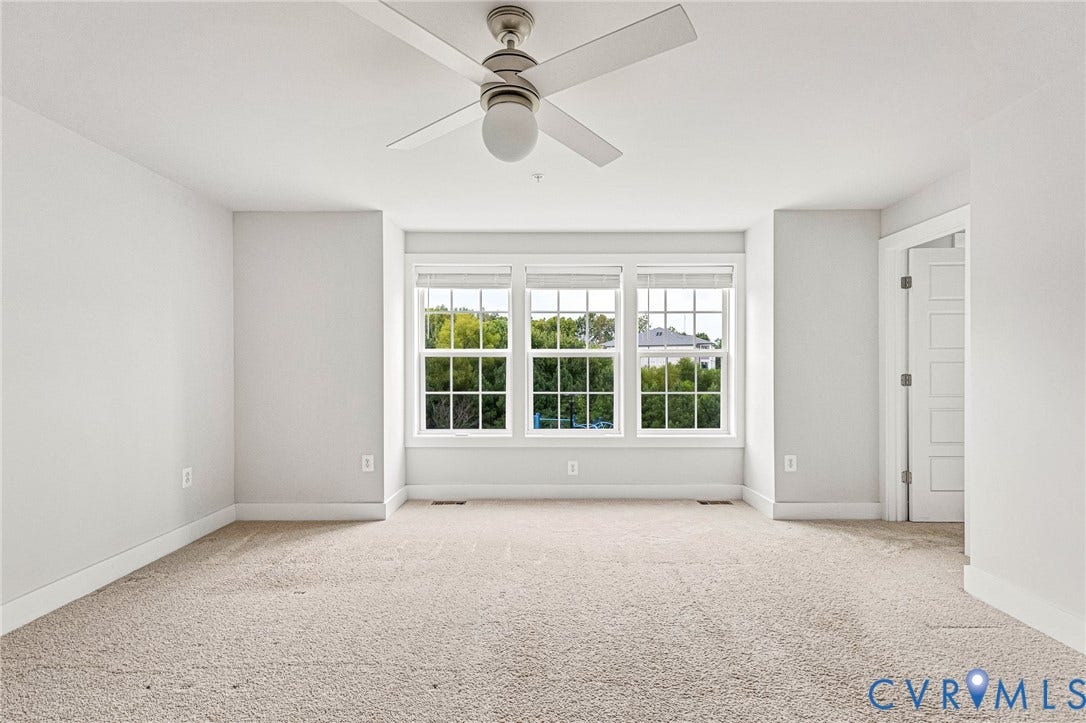 4347 Saunders Station Loop, #A, Glen Allen, VA 23233 Bright, airy bedroom showcasing abundant natural light through triple-pane bay windows, neutral wall finishes, neutral carpeting, and a ceiling fan with integrated lighting