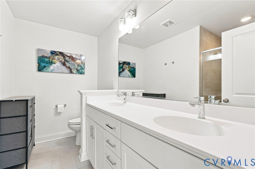 13820 Village View Drive, Midlothian, VA 23114 Dual vanity with integrated sinks and chrome fixtures, white cabinetry with silver-tone hardware, full-width mirror, and a tiled shower enclosure with a glass door