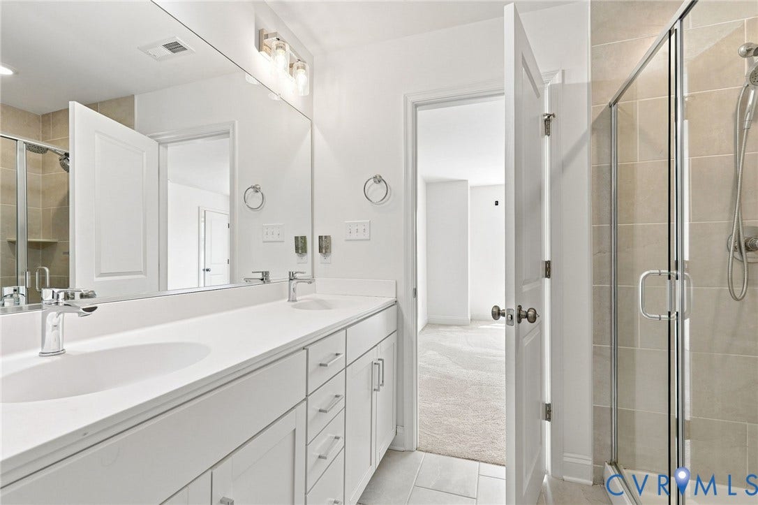 13820 Village View Drive, Midlothian, VA 23114 Dual vanity with white cabinetry and integrated sinks, a large wall-mounted mirror, and a glass-enclosed shower with tiled walls