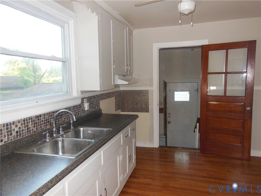 5307 Media Road, Richmond, VA 23225 White cabinetry with brushed nickel hardware, mosaic tile backsplash, black countertop, double basin stainless steel sink with chrome faucet, and wood-finish flooring