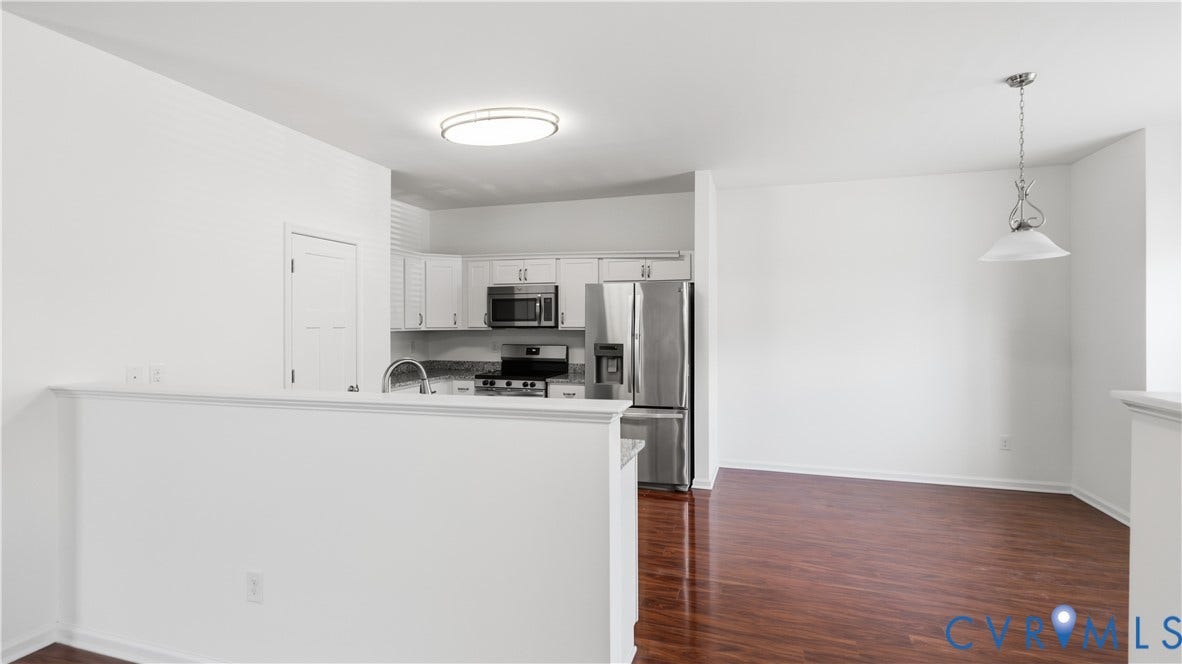 Open-concept living area featuring a half-wall kitchen partition, stainless steel appliances including a refrigerator and range, wood-finish flooring throughout, recessed ceiling lighting, and pendant lighting fixture