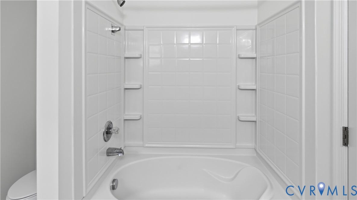 White tub/shower combination with chrome fixtures, tiled surround, and integrated shelving