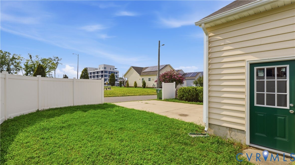 White privacy fencing, manicured lawn, concrete driveway, beige horizontal siding, and a green door with window panes