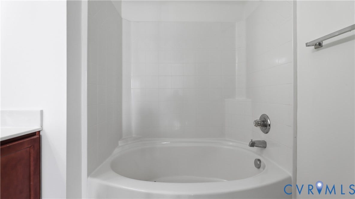 Corner tub with tiled surround, chrome fixtures, and adjacent vanity with white countertop