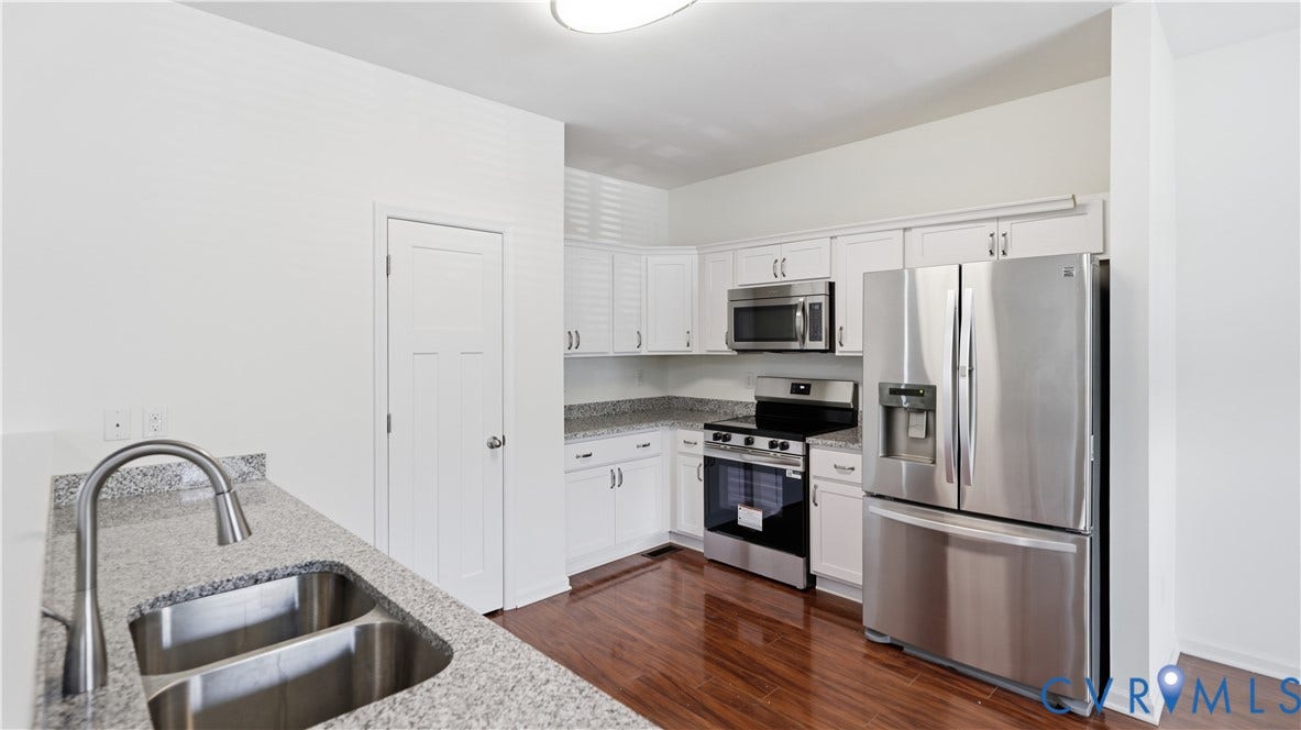 Kitchen featuring white cabinetry, stainless steel appliances, a double basin sink with a gooseneck faucet, light-colored countertops, and wood-finish flooring