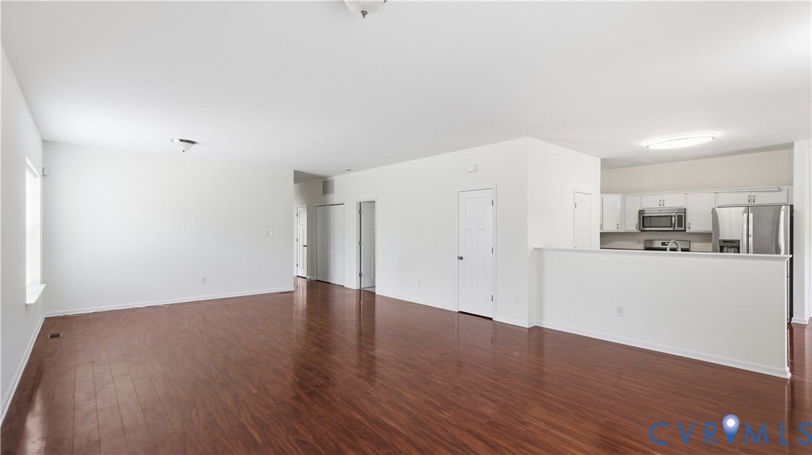 Expansive wood-finish flooring throughout, bright white walls, recessed lighting, and kitchen featuring stainless steel appliances