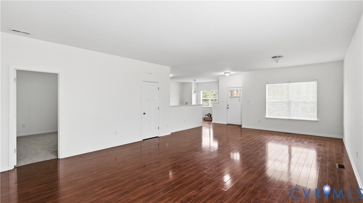 Expansive room featuring wood-finish flooring, white walls, multiple windows with blinds, and white trim