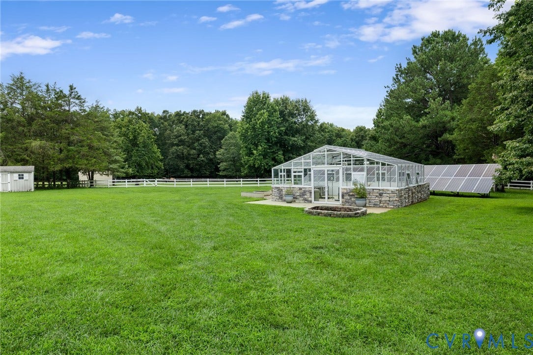 2365 Manakintown Ferry Road, Powhatan, VA 23113 Expansive lawn featuring a greenhouse with a stone base, an integrated fire pit, solar panels, and a white fence
