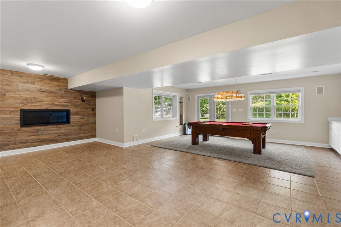 2365 Manakintown Ferry Road, Powhatan, VA 23113 Spacious interior featuring a wood-finish accent wall, built-in linear fireplace, tile flooring, and multiple windows with outdoor access