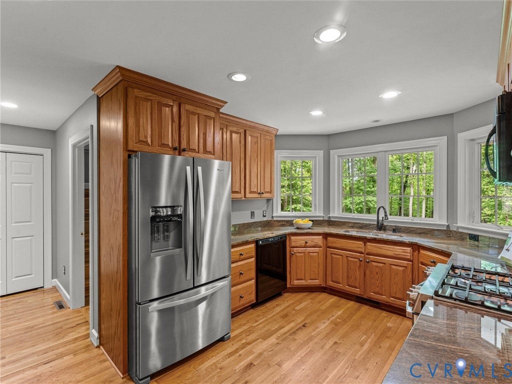 Kitchen featuring wood cabinetry, stainless steel appliances, a bay window, recessed lighting, and wood-finish flooring