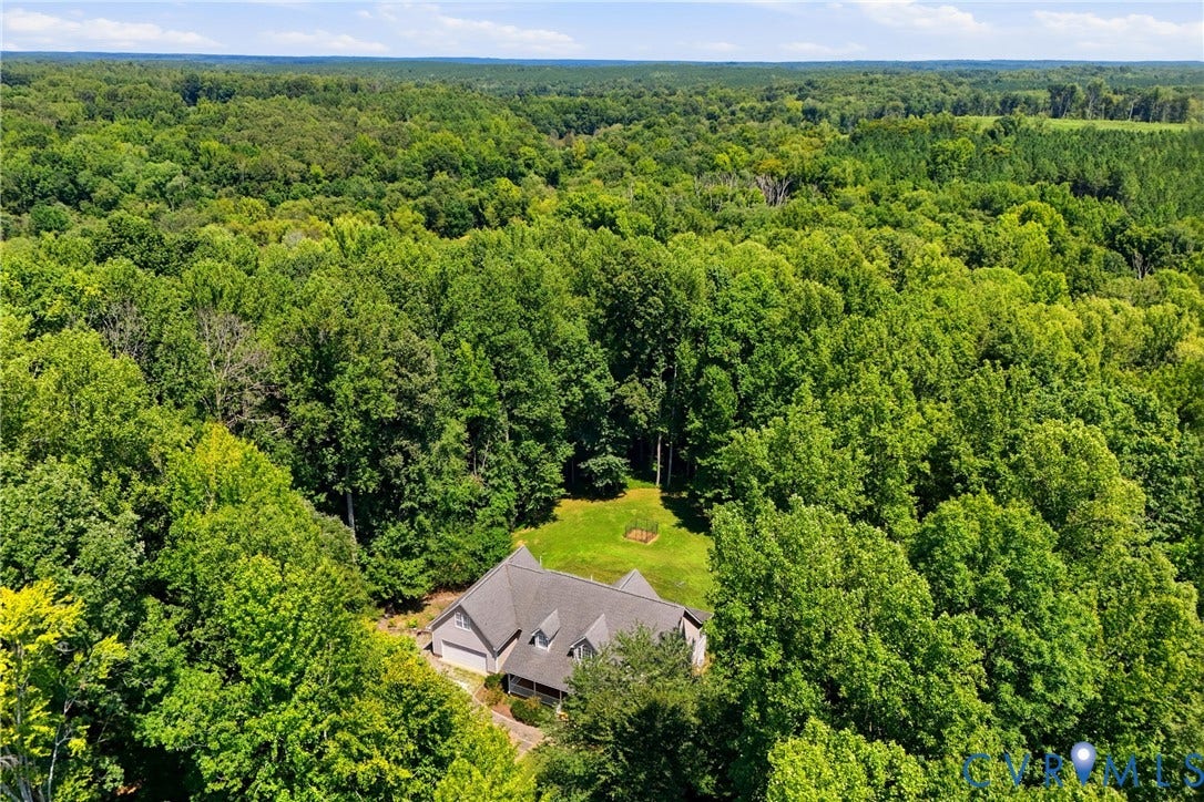 Extensive wooded acreage surrounding a residence with a gray roof and a green lawn