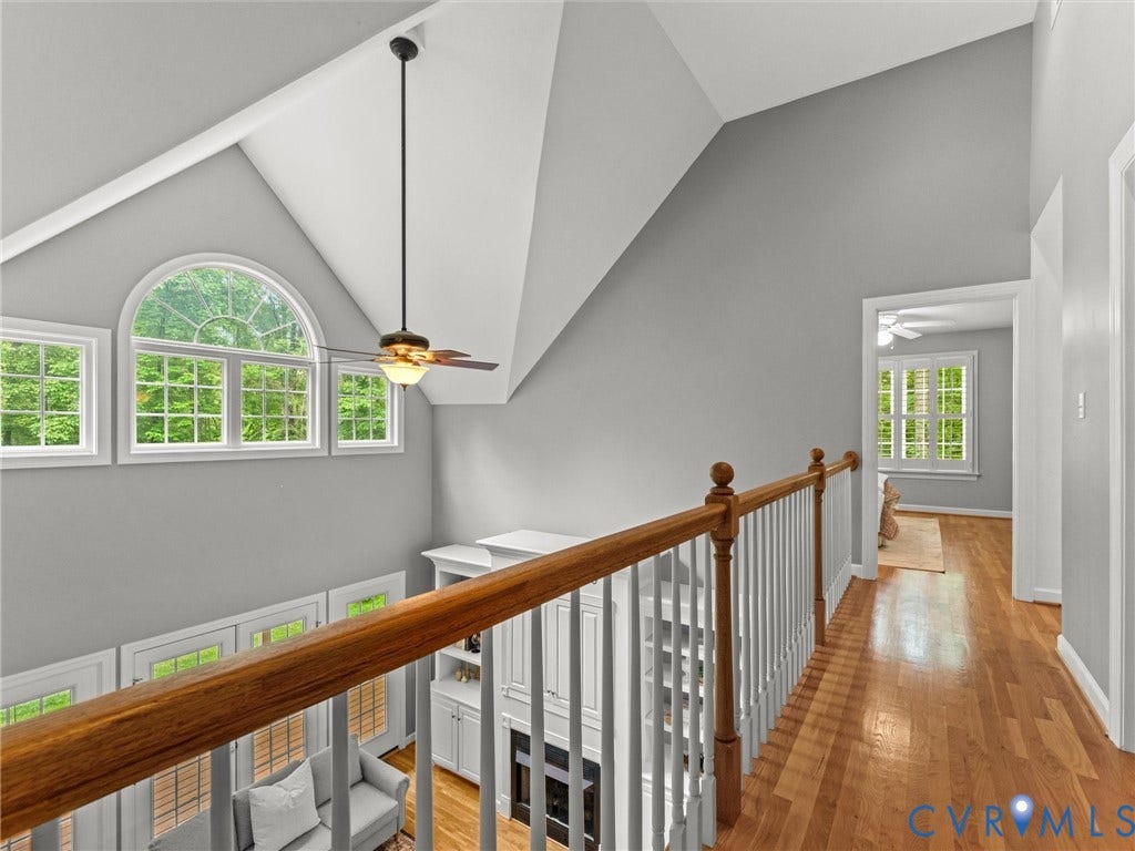 Vaulted ceiling with a suspended ceiling fan, arched transom window, wood-finish flooring, and white railing with a wood-finish handrail
