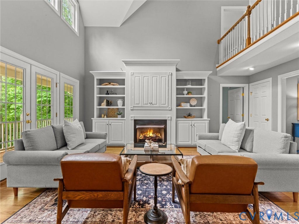 Two-story living area featuring a fireplace with built-in shelving, wood-finish flooring, and multiple glass-paned doors