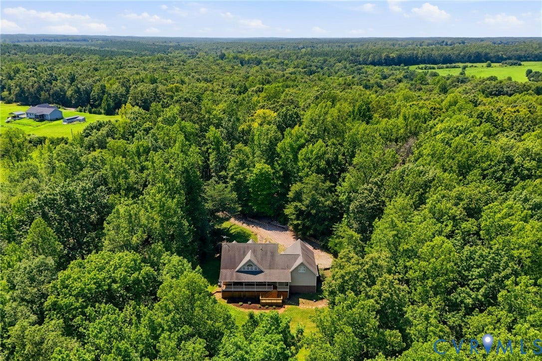 Expansive treed landscape featuring a gabled roofline, covered porch, and surrounding greenery