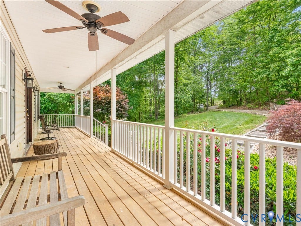 Expansive covered porch featuring wood-finish decking, white railings, and multiple ceiling fans