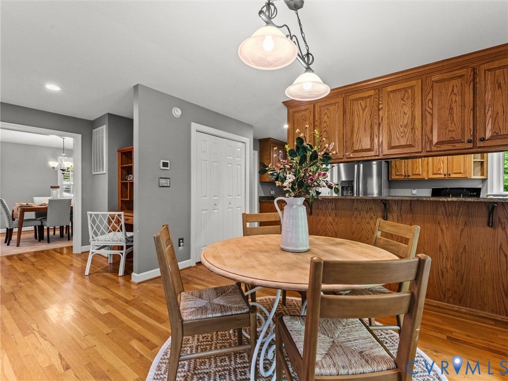 Hardwood flooring throughout, overhead pendant lighting, wood cabinetry with black hardware, and a breakfast bar with stone-finish countertop
