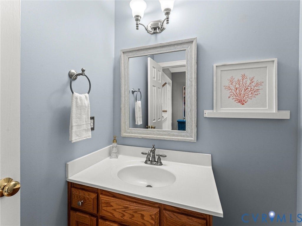 Wood-finish vanity with a white countertop and undermount sink, complemented by a distressed white framed mirror and wall-mounted vanity lighting