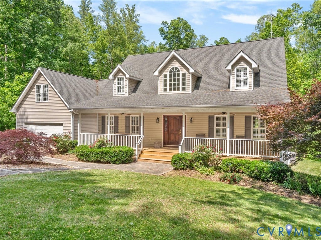 Classic Colonial-style home featuring a welcoming front porch with white railings, peaked roofline with multiple dormers, and a blend of siding and stone exterior finishes