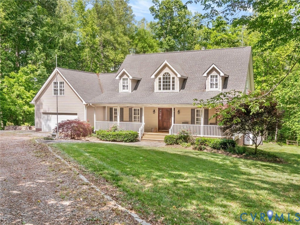 Gabled roofline with dormer windows, covered front porch, wood-paneled entry door, attached garage, and a gravel driveway