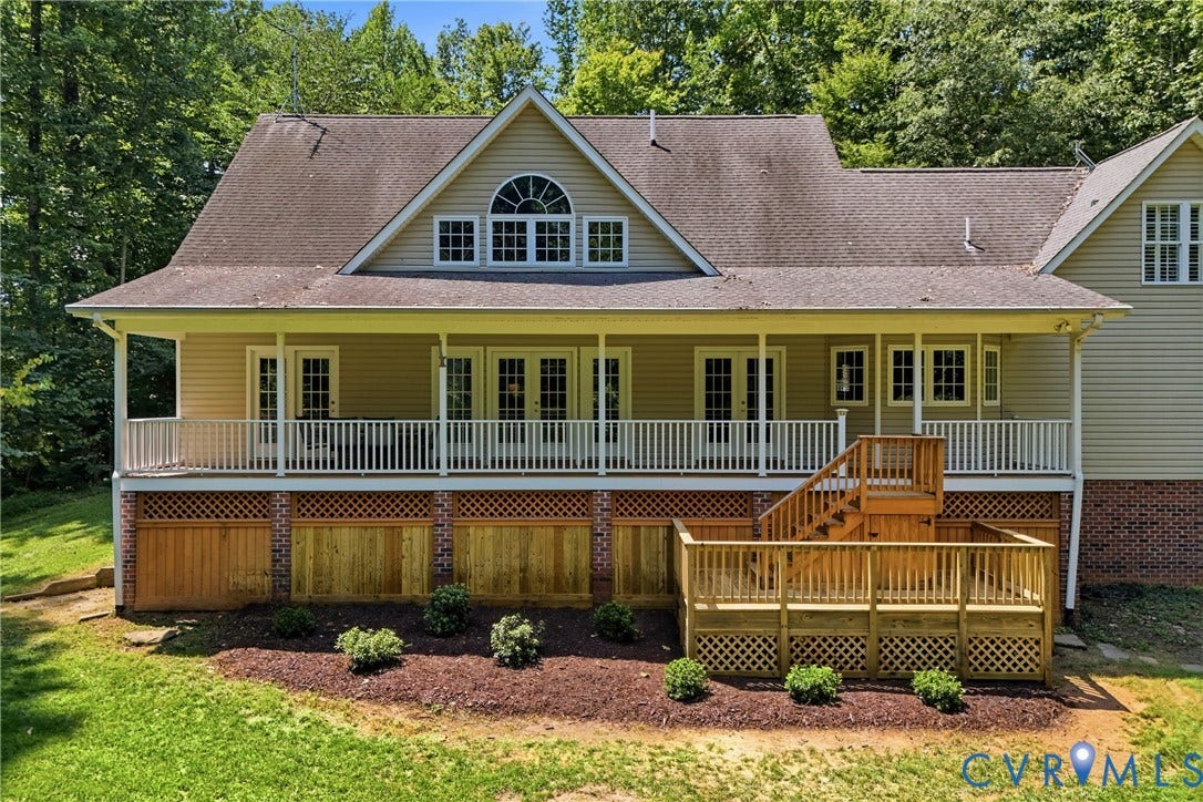 Expansive rear facade featuring a full-length covered porch, multiple French doors, a gabled roofline with an arched window, and a multi-level wood deck