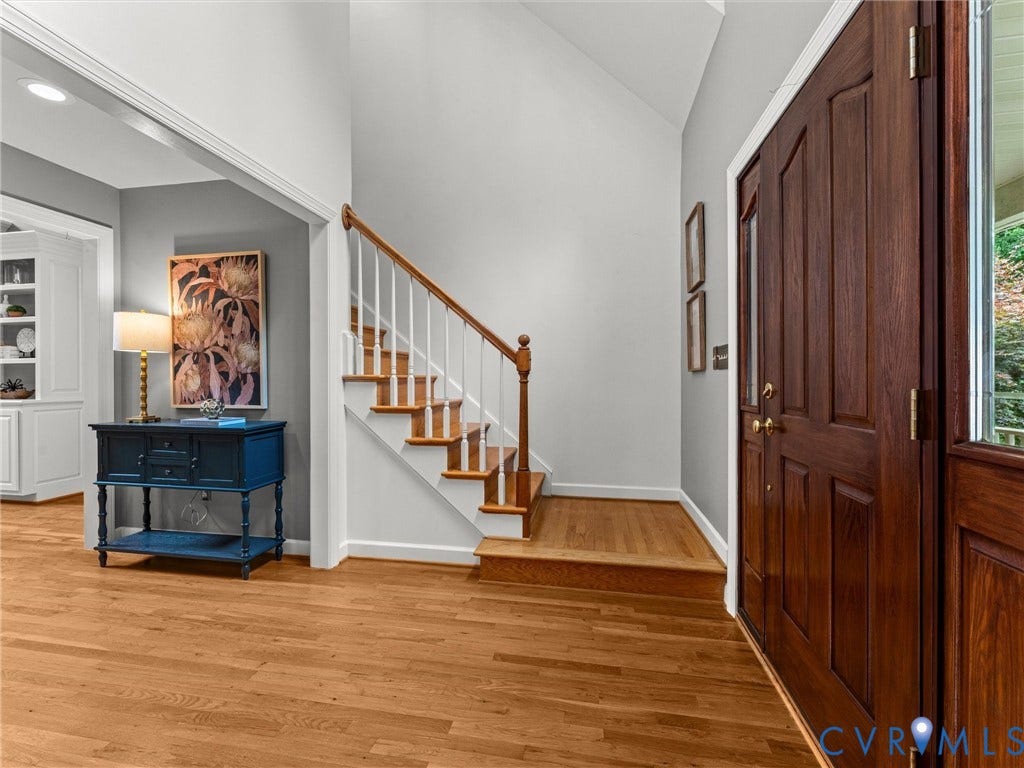 Hardwood flooring, wood staircase with white risers, wood banister with white spindles, double-panel wood door, and built-in white cabinetry