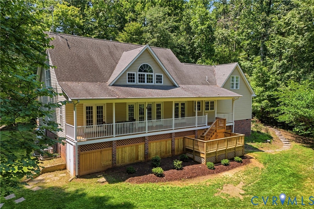 Traditional residence featuring a covered porch with white railings, a multi-level wood deck, and a dormer with an arched window