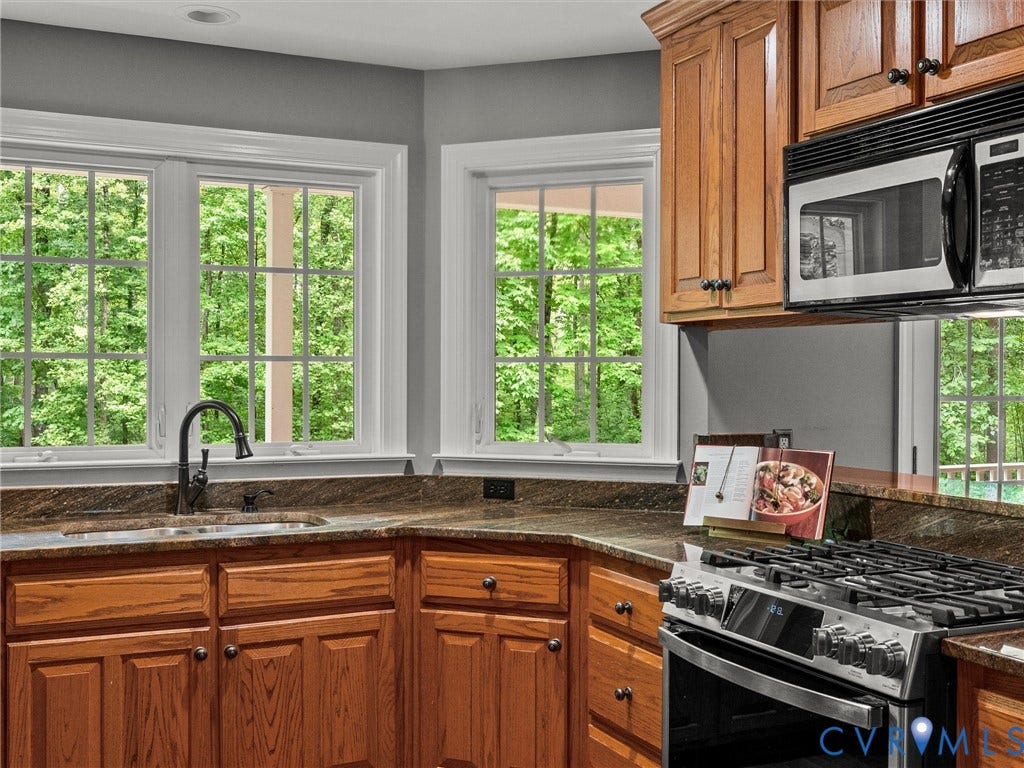 Wood cabinetry with dark hardware, stone countertops, stainless steel gas range, and undermount sink with a gooseneck faucet