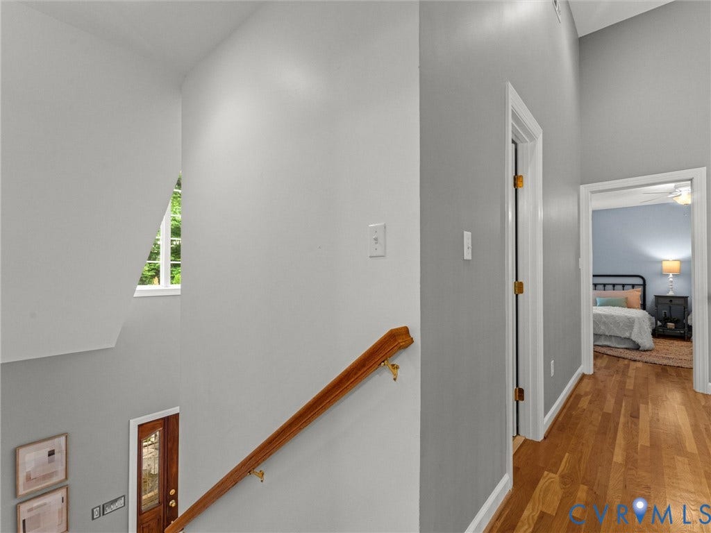 Bright stairwell with wood-finish handrail and treads, white walls, and natural light from a high window
