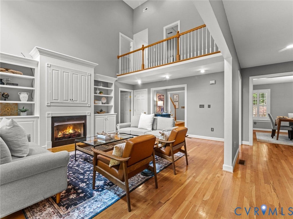 Hardwood flooring throughout, vaulted ceiling, built-in shelving, fireplace with mantel, and an upper-level balcony with wood railing