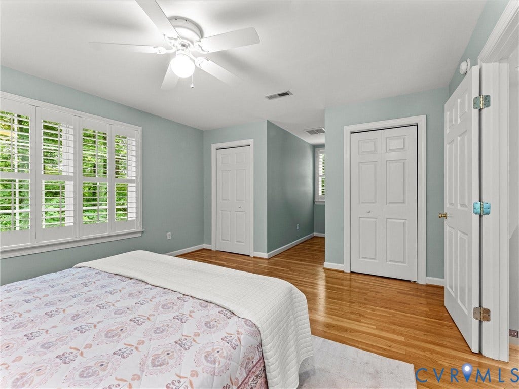 Hardwood flooring, plantation shutters, ceiling fan with light fixture, and white bi-fold closet doors