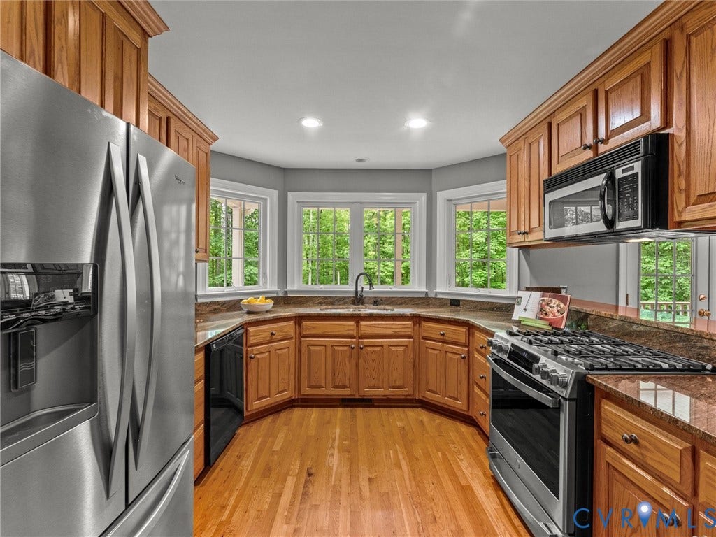 Stainless steel appliances, wood-finish flooring, recessed lighting, wood cabinetry, and a curved countertop