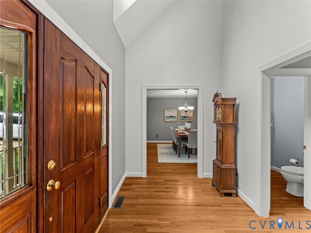 Elegant foyer showcasing rich wood-finish double doors with brass hardware, gleaming hardwood flooring, and bright, open architecture