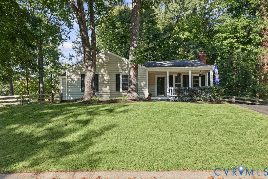 13512 Master Stag Drive, Midlothian, VA 23112 Single-story residence featuring light-colored horizontal siding, a covered front porch, dark shutters, and white post-and-rail perimeter fencing situated on a wooded lot