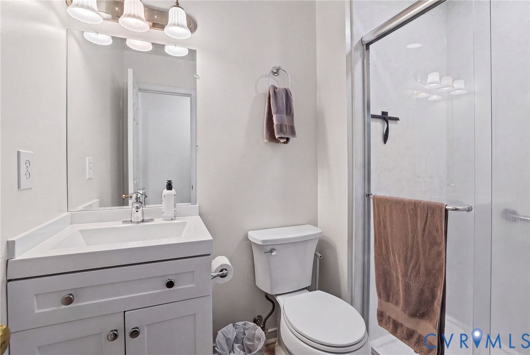 13512 Master Stag Drive, Midlothian, VA 23112 Bathroom featuring a white vanity cabinet with a stone countertop, integrated sink, large wall-mounted mirror, polished chrome fixtures, and a glass-enclosed shower