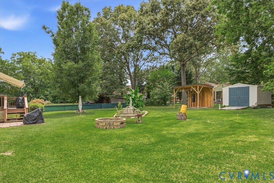 13308 S Chester Road, Chester, VA 23831 Expansive manicured lawn anchored by a stone fire pit, surrounded by mature shade trees and multiple outbuildings including a pool house and garden structures