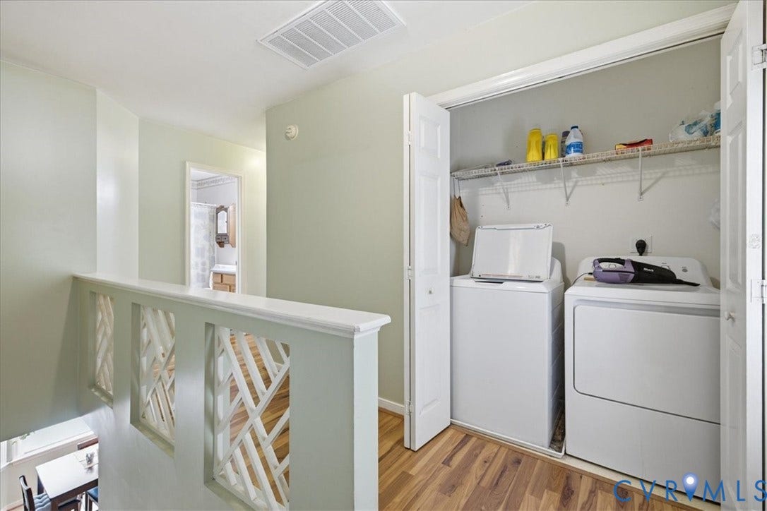 13308 S Chester Road, Chester, VA 23831 Dedicated laundry room featuring white front-load washer and dryer, wood-finish flooring, built-in cabinetry with open shelving for storage, and soft sage-green walls with crisp white trim