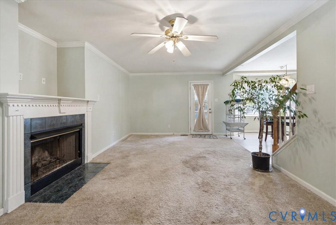 13308 S Chester Road, Chester, VA 23831 Spacious living area featuring neutral carpet flooring, a gas fireplace with decorative surround and mantelpiece, ceiling fan with integrated lighting, and glass sliding doors providing natural light