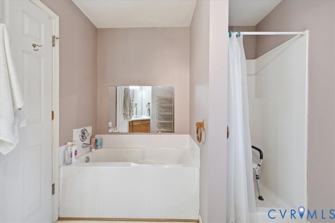 13308 S Chester Road, Chester, VA 23831 Spa-inspired primary bathroom featuring a deep soaking tub with integrated surround, dual vanity with ample counter space, large framed mirror, and a separate walk-in shower enclosure with glass partition and white subway tile surround