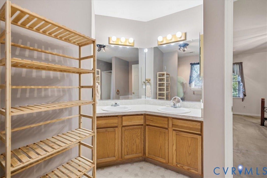 13308 S Chester Road, Chester, VA 23831 Master bathroom featuring a dual-sink vanity with wood cabinetry, large framed mirror with integrated lighting, and marble countertop