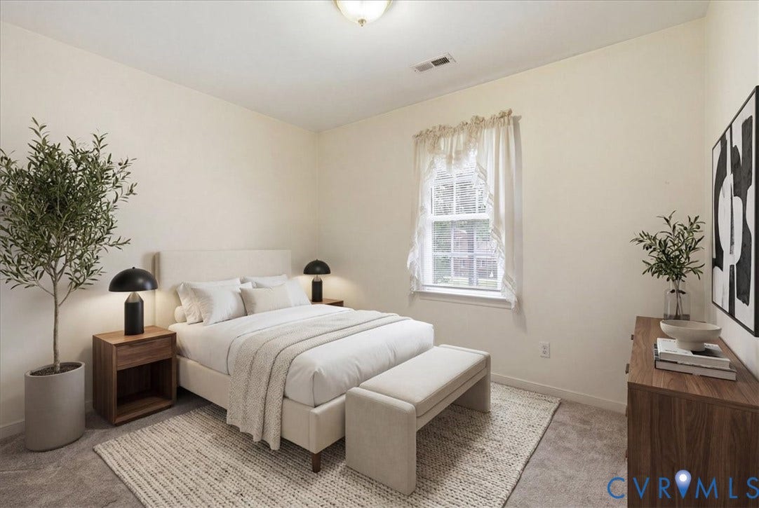 13308 S Chester Road, Chester, VA 23831 Serene primary bedroom showcasing neutral wall finishes, abundant natural light from a large window with sheer curtains, wood-finish nightstands with integrated lighting, and neutral-toned area rugging