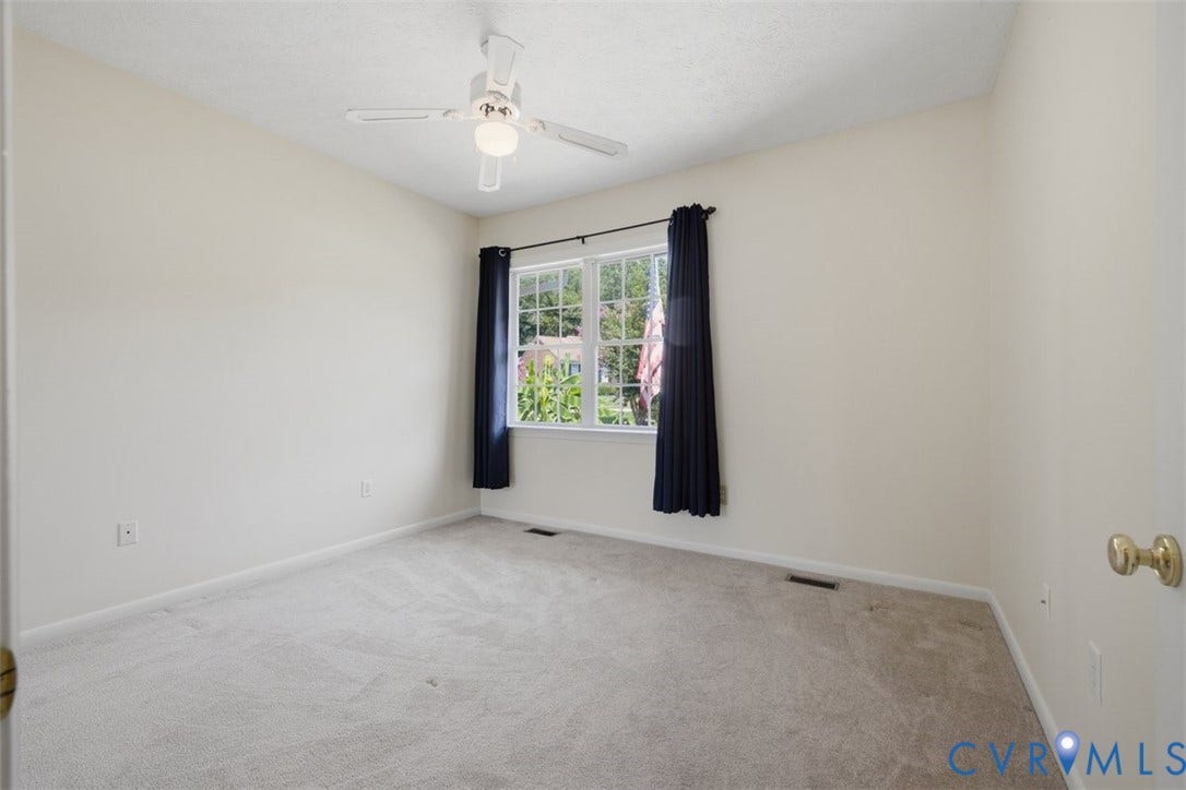 12600 Lilking Road, Chester, VA 23831 Bright secondary bedroom featuring carpet flooring, a ceiling fan with integrated lighting, and a large double-hung window with black curtain rods framing natural light and outdoor greenery