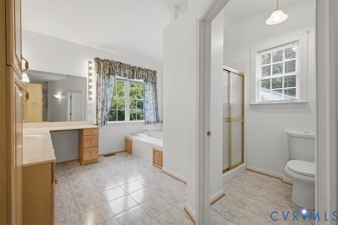 12600 Lilking Road, Chester, VA 23831 Primary bathroom suite featuring a soaking tub with wood-finish cabinetry, dual vanity with ample counter space, ceramic tile flooring, a separate walk-in shower with brushed brass framing, and a toilet compartment