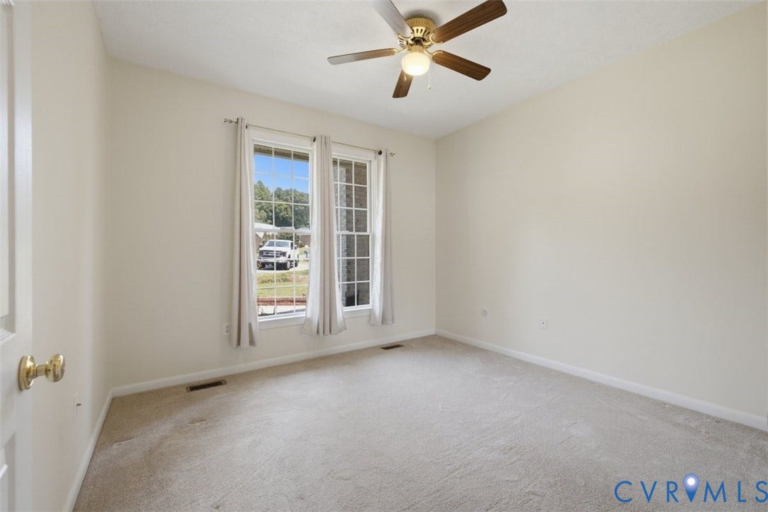 12600 Lilking Road, Chester, VA 23831 Bright, carpeted bedroom featuring glass French doors with transom windows, ceiling fan with brass fixture, and natural light from dual glass panels overlooking the exterior grounds