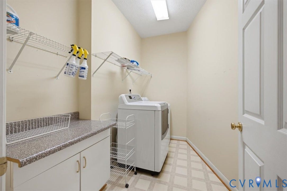 12600 Lilking Road, Chester, VA 23831 Dedicated laundry room featuring ample cabinetry with brushed gold hardware, speckled quartz countertop workspace, wall-mounted shelving for storage, ceramic tile flooring, and bright overhead lighting
