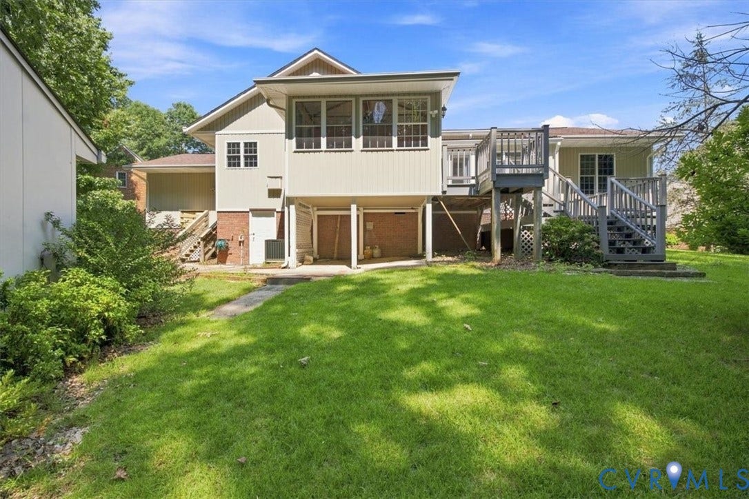 12600 Lilking Road, Chester, VA 23831 Spacious rear yard with mature landscaping and lush lawn, anchored by a two-story residence featuring brick and siding exterior, elevated deck with railings, and attached garage