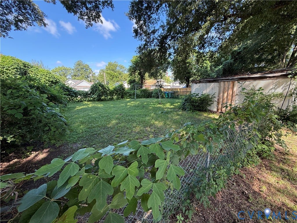 1313 Enfield Avenue, Richmond, VA 23224 Expansive green lawn, mature perimeter trees, chain-link fencing, and an outbuilding with a corrugated metal roof
