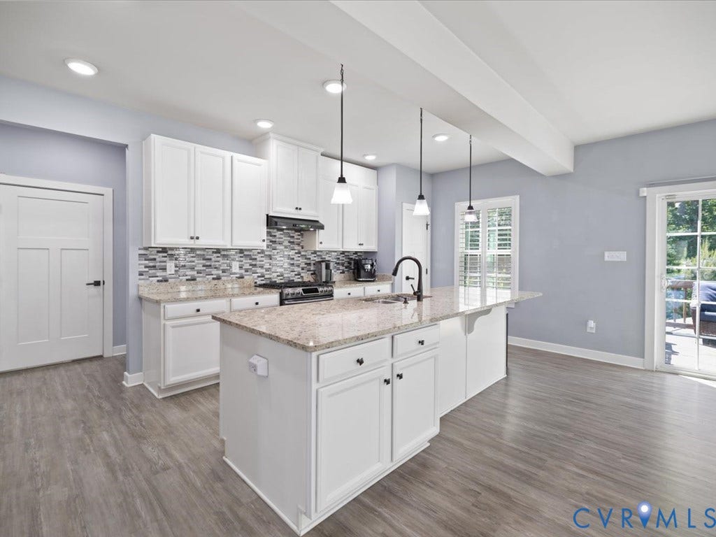 Kitchen featuring wood-finish flooring, white cabinetry, a central island with a granite countertop, and a tile backsplash